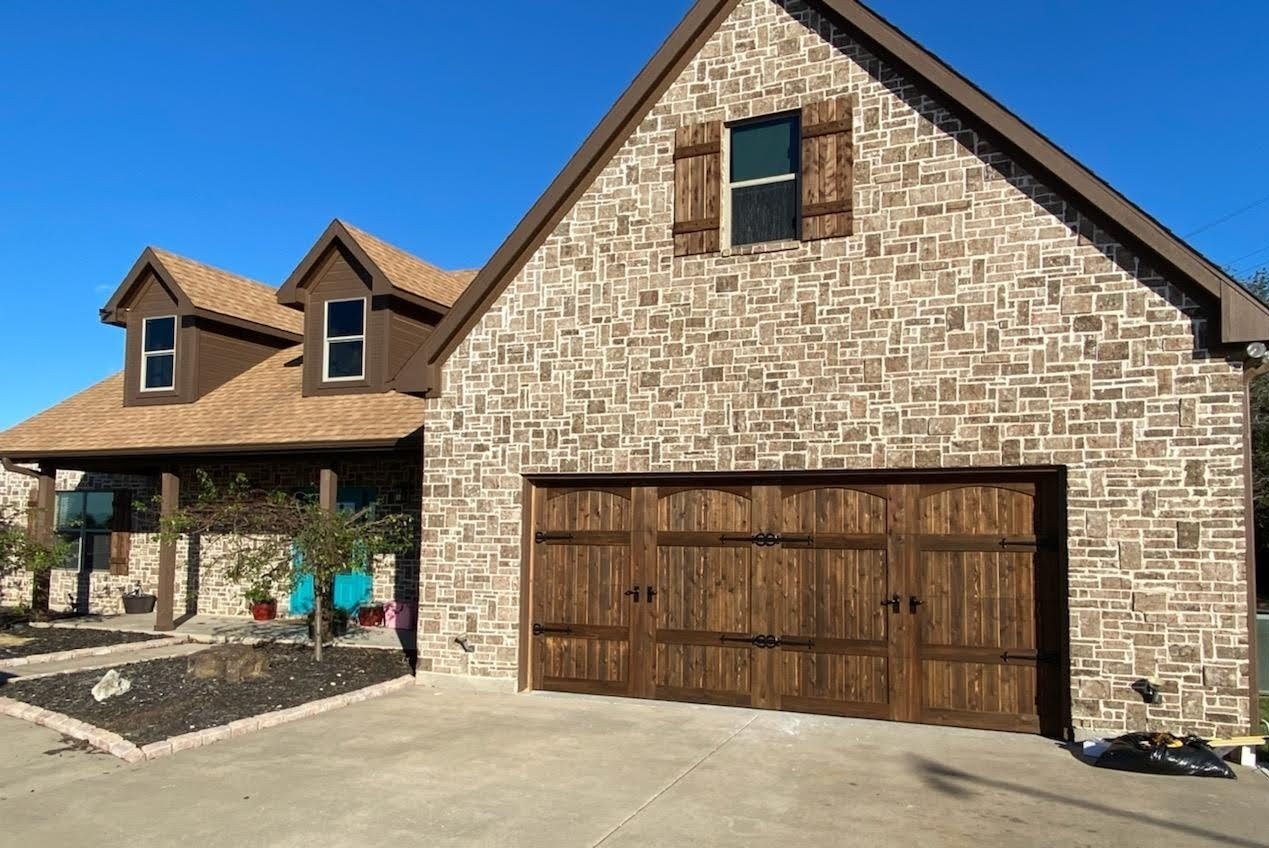 Stone home with dark stained arched carriage wood garage doors